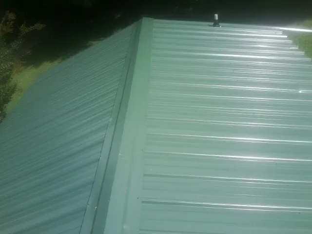 New green metal panels meeting at the ridge of a roof — Flat Roof Repair work by our crew in Millville